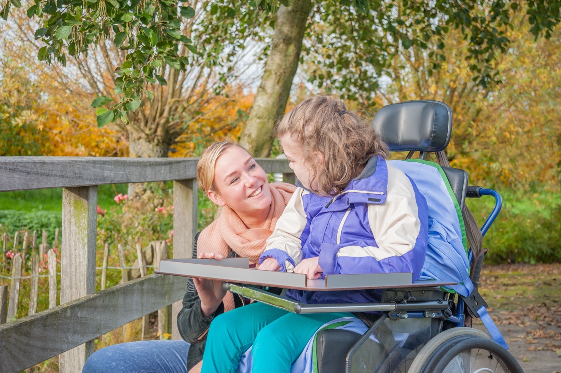 A girl in a wheelchair, working with a woman on a board.